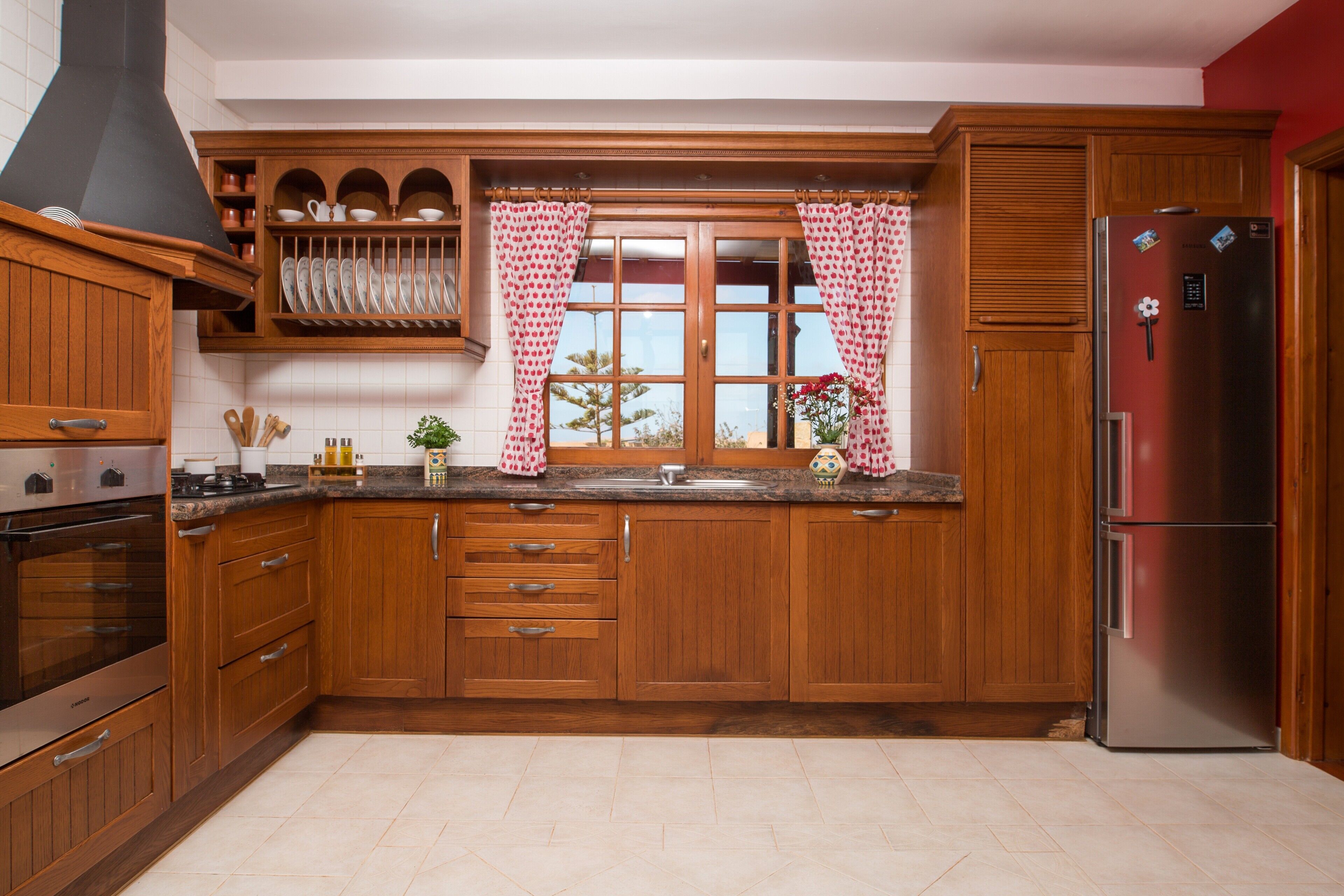 Eine Küche mit Holzschränken, einem Edelstahlkühlschrank und einem Fenster mit karierten Vorhängen.