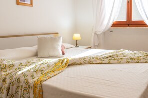 Un lit bien fait, recouvert d’une couverture à motifs, une lampe de chevet et une fenêtre avec des rideaux.