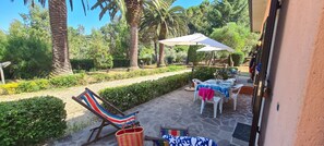 Une terrasse extérieure avec une table et des chaises, un fauteuil de jardin à rayures et un grand parasol.