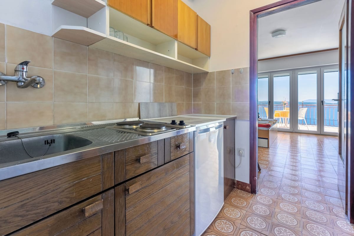 A modern kitchen with a stainless steel countertop, wooden cabinets, and a view of a balcony with outdoor seating.