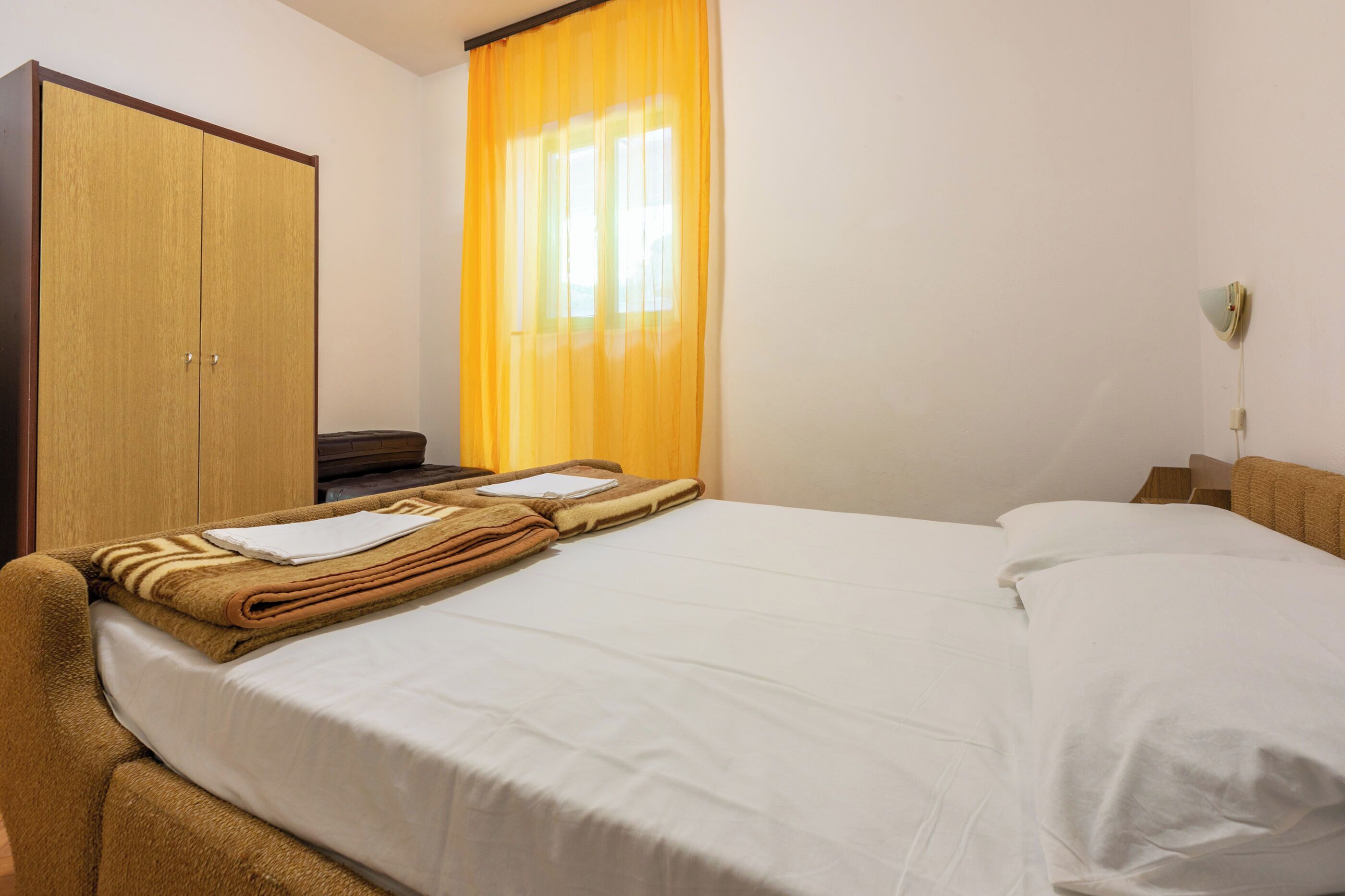 Een hotelkamer met een bed, een kledingkast, een bureau en een raam met gordijnen.