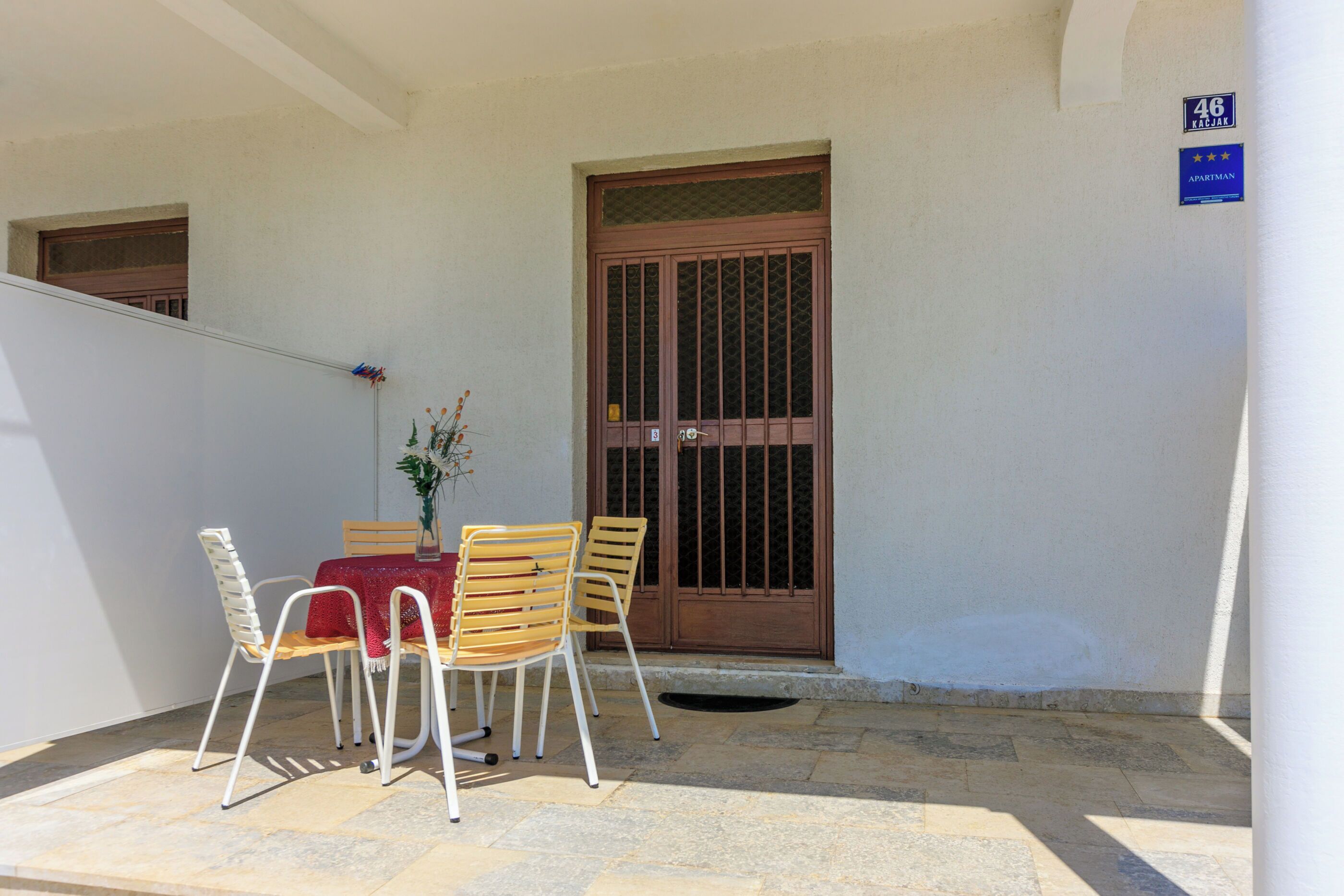 Un pequeño espacio al aire libre con mesa y sillas, una planta en maceta y una puerta con reja.