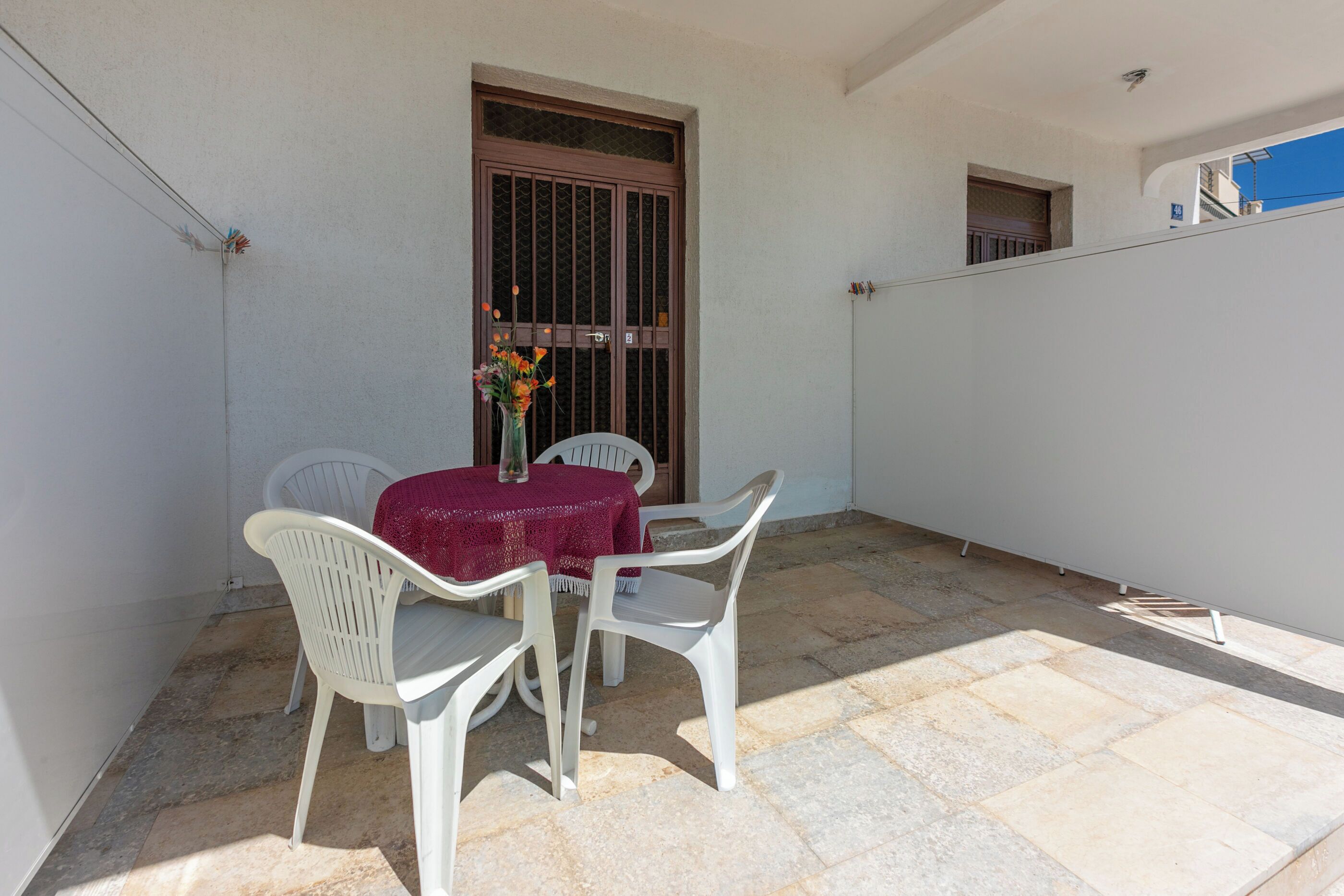 Une petite terrasse extérieure avec une table et des chaises, un vase rempli de fleurs et une porte dotée d’une fenêtre.