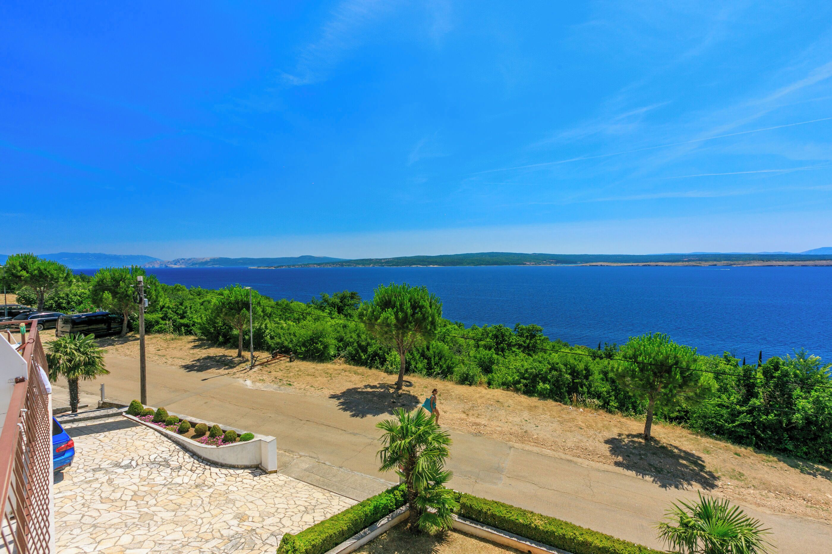 A coastal view with a paved area, trees, and a clear blue sky.
