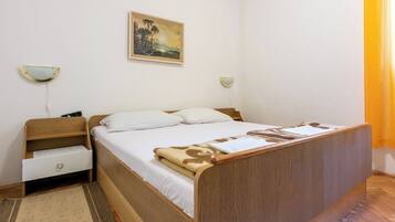 A bedroom with a wooden bed, white bedding, a small bedside table with a lamp, and a painting on the wall.