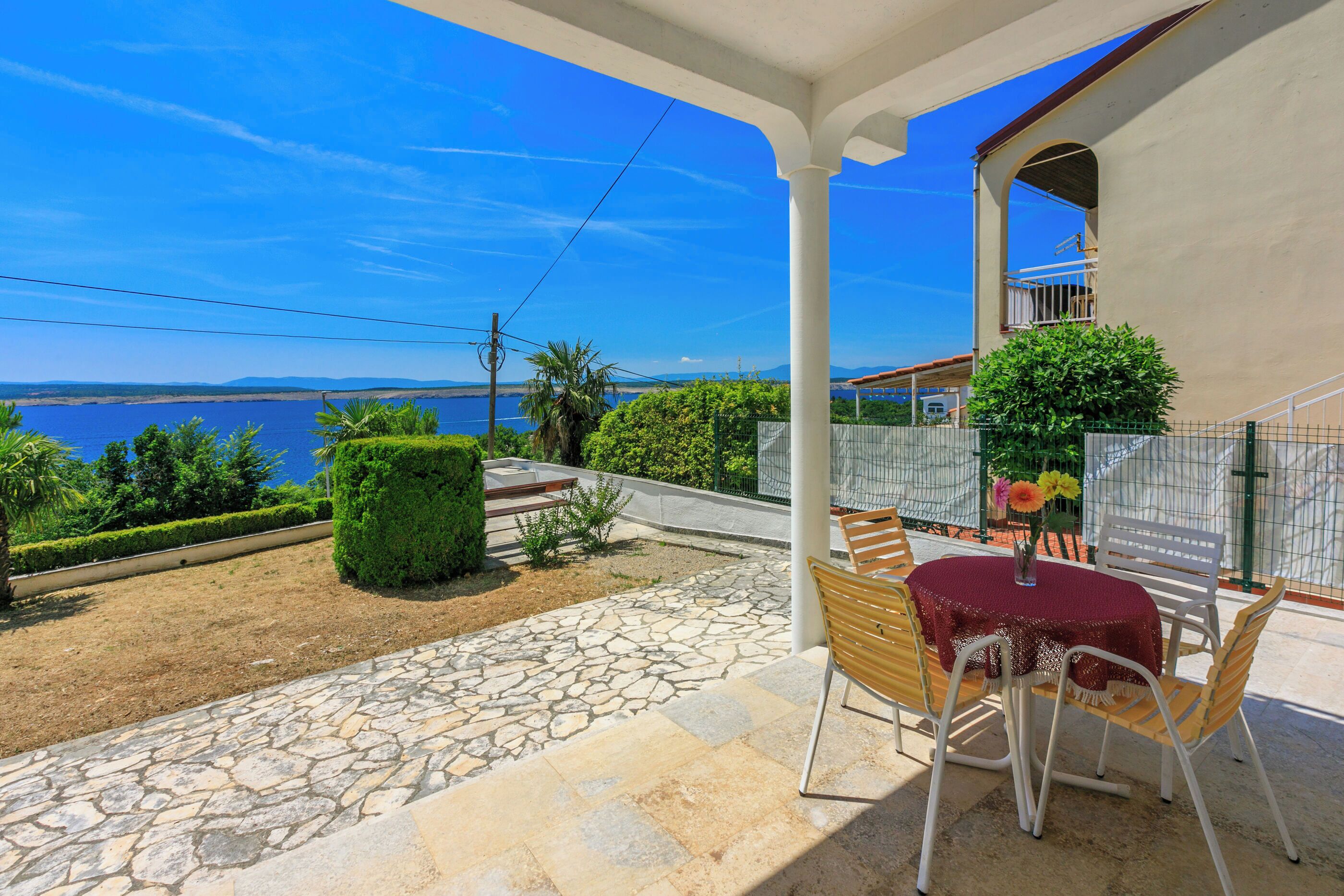 A patio with stone flooring, a round table with chairs, and a view of the sea.
