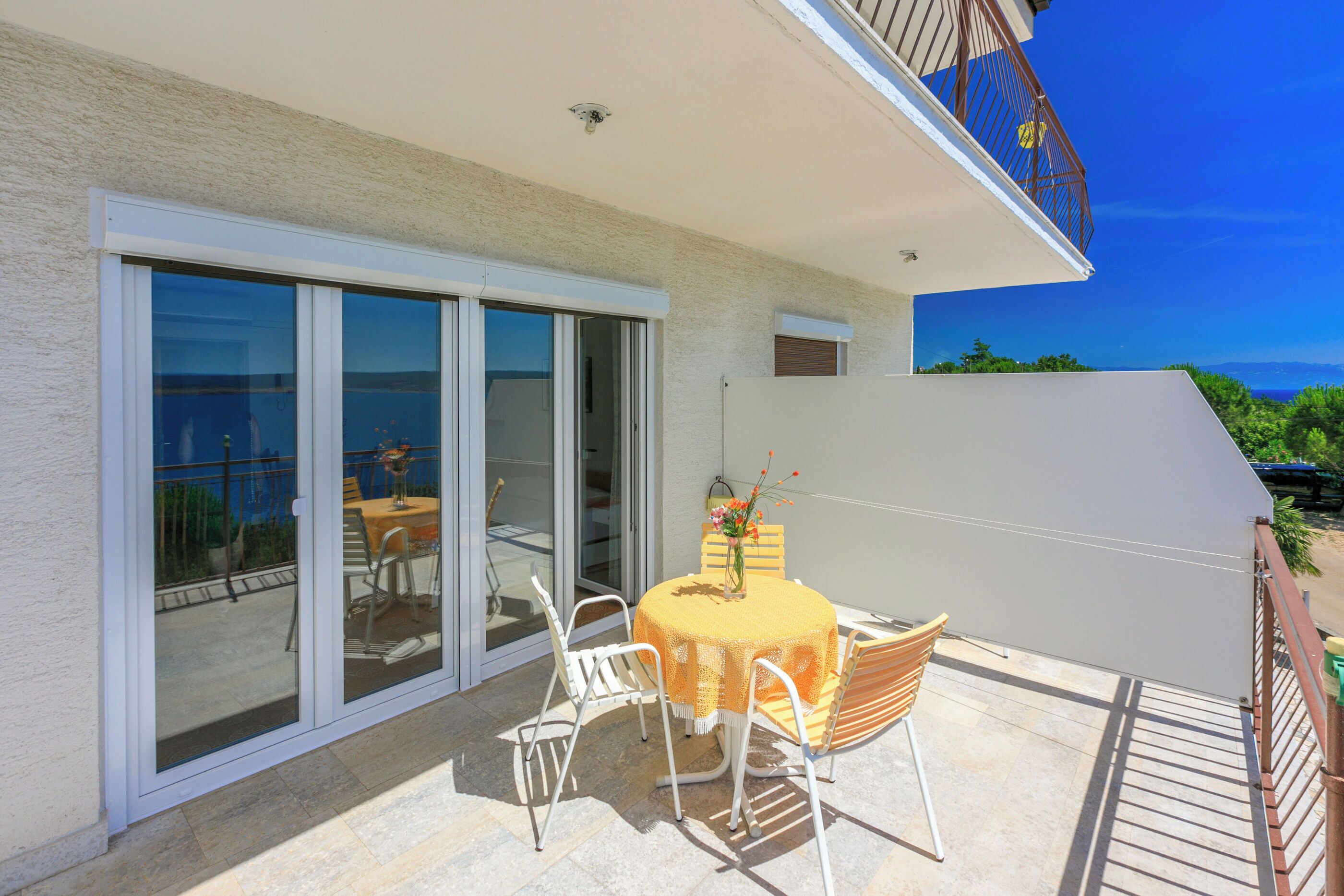 A balcony with a table and chairs, a sliding glass door, and a view of the ocean.