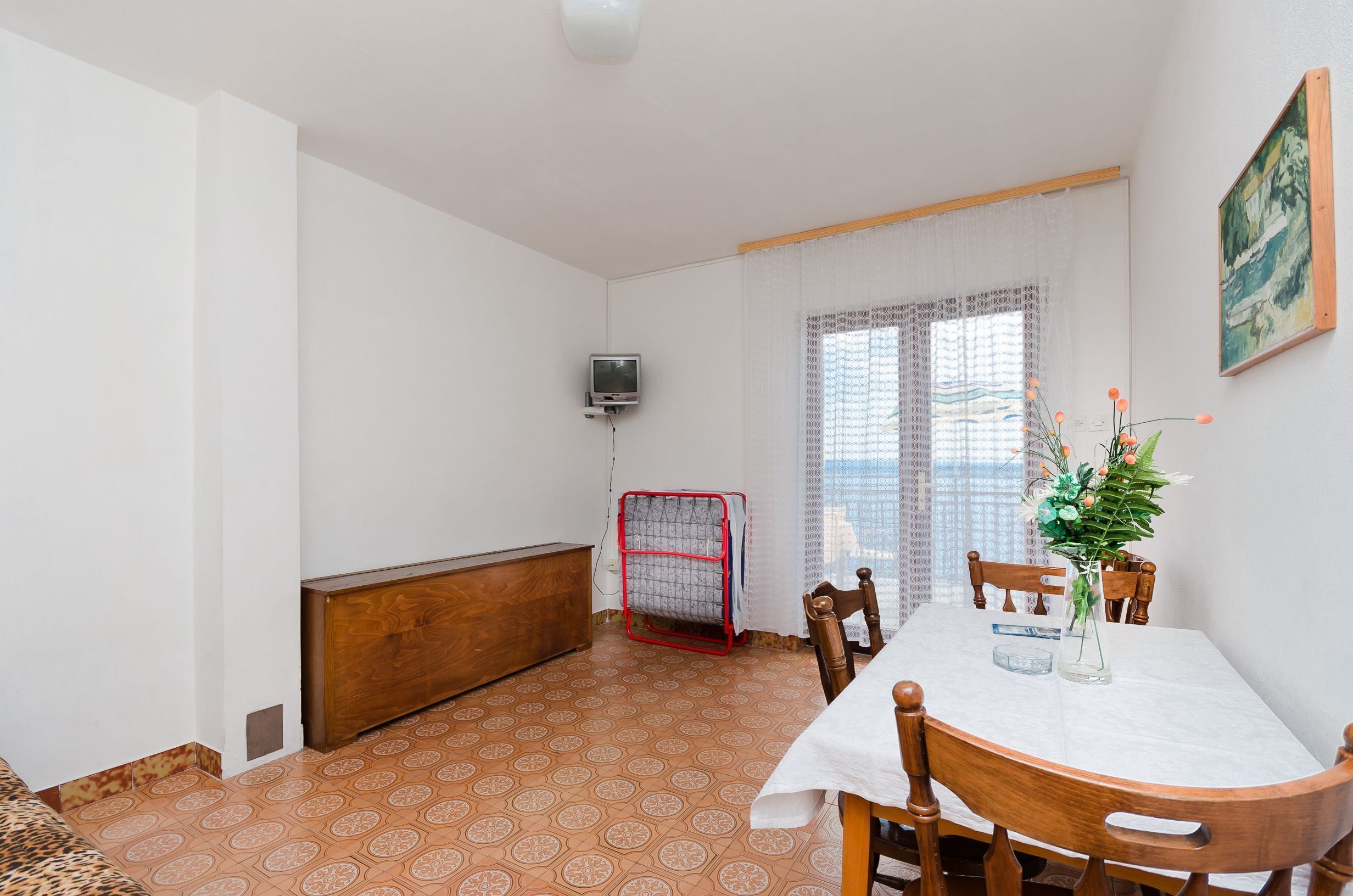 A dining area with a table, chairs, a TV, a radiator, and a window with curtains.