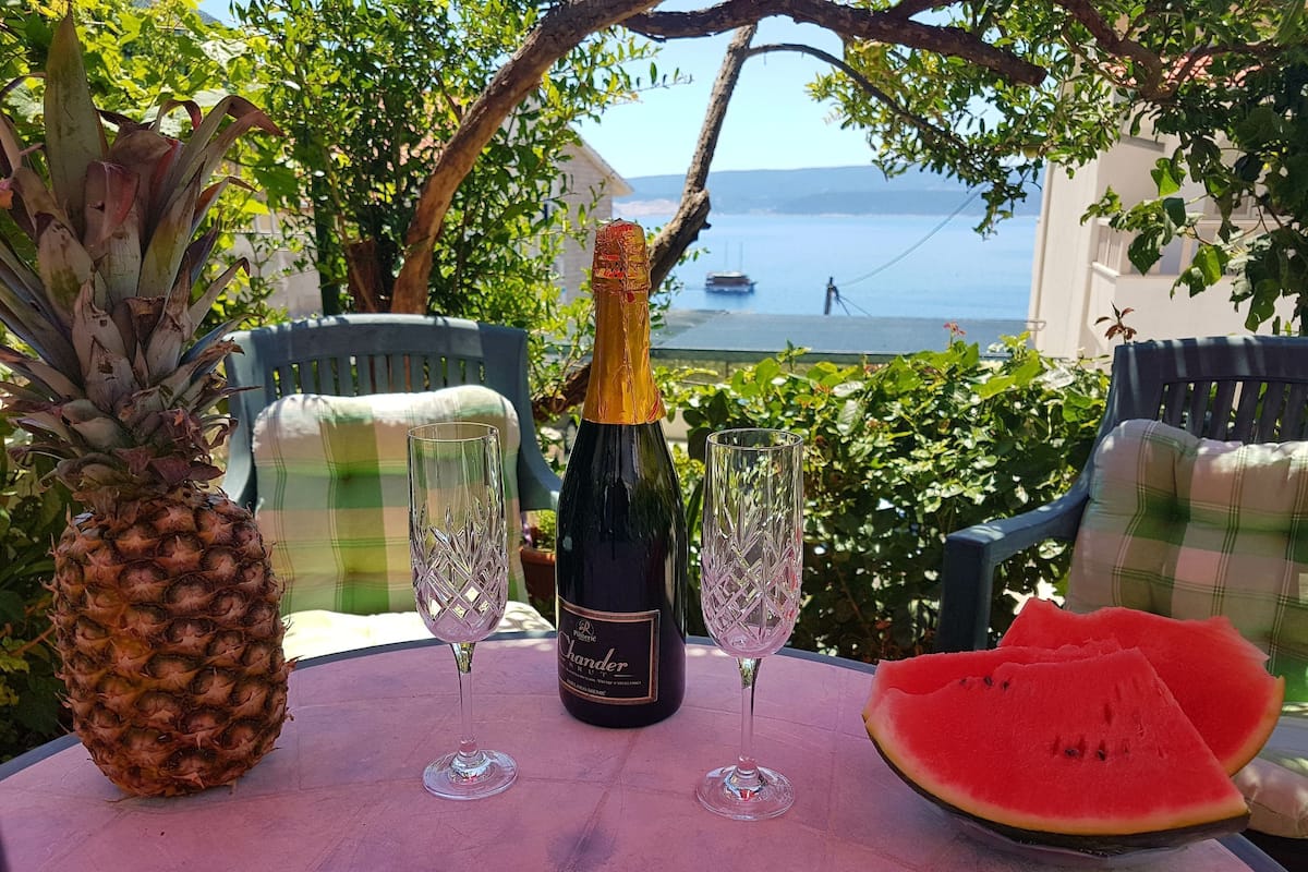 Une table avec une bouteille de vin, deux verres, un ananas et une tranche de pastèque.