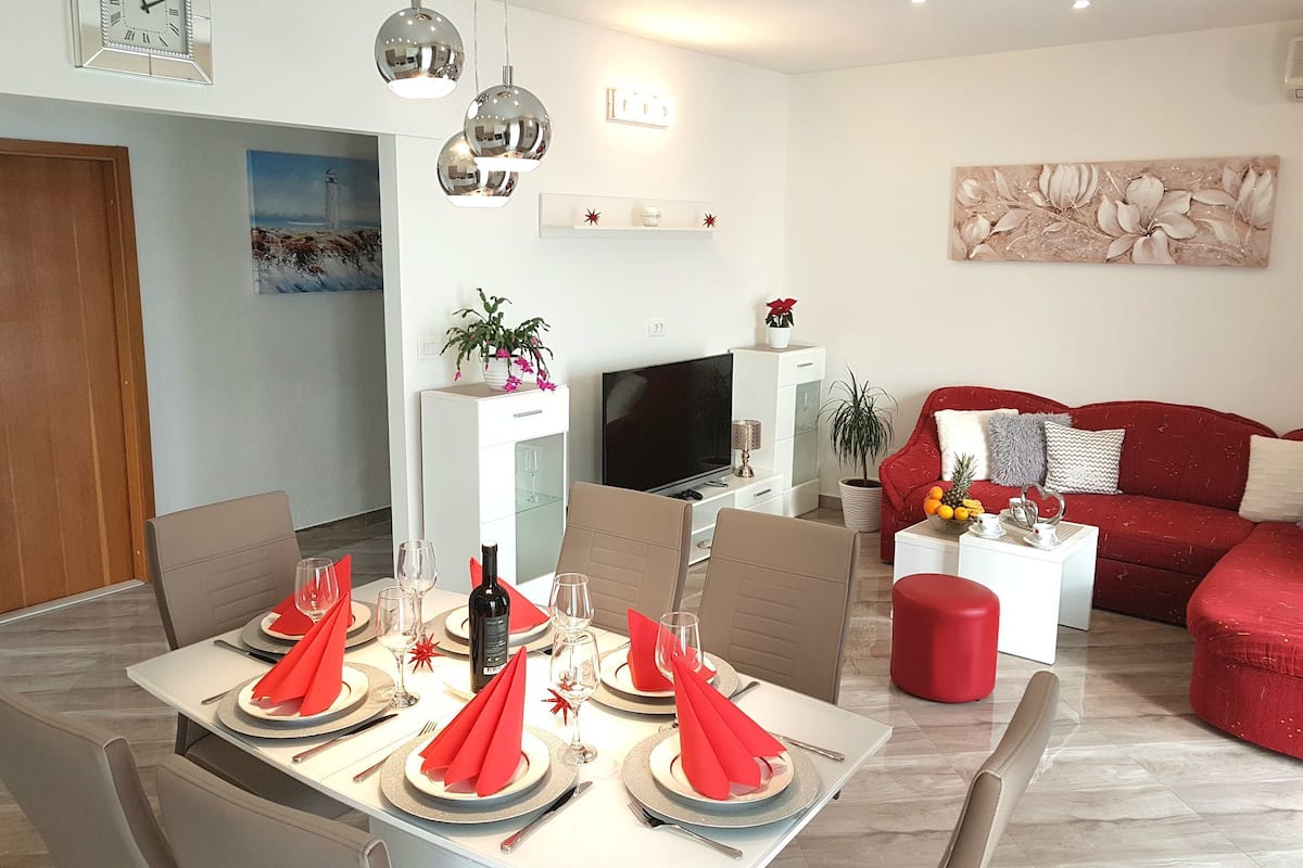 Un salon moderne avec un canapé rouge, un coin repas avec une table dressée et un téléviseur en arrière-plan.