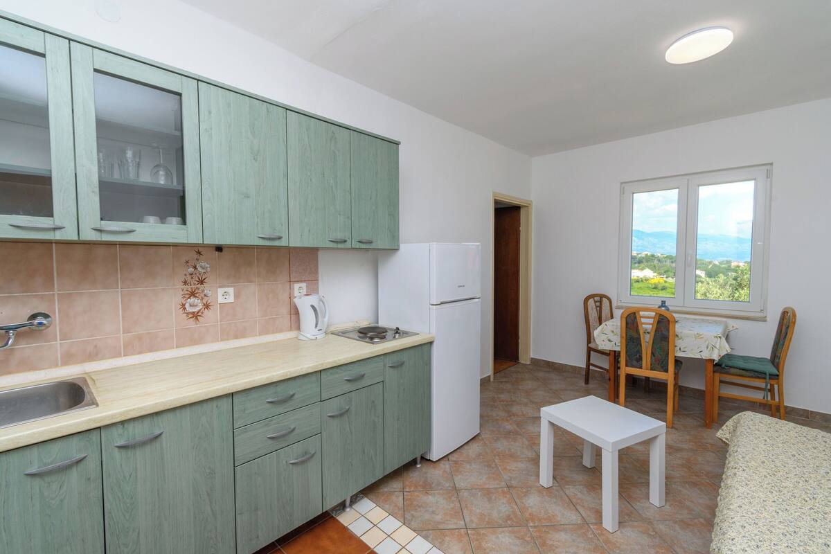 Una cocina con gabinetes verdes, un refrigerador blanco, un lavamanos y un ventanal con vistas.
