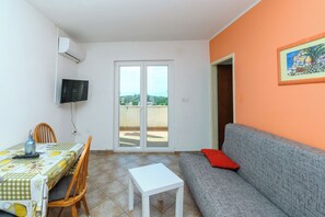 A room with a dining table, chairs, a sofa, a TV, and a sliding glass door leading to a balcony. - Apartments Sime (Lopar)