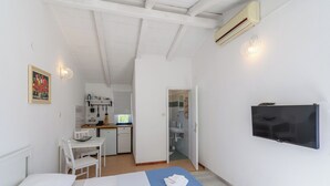 Un dormitorio con cama, escritorio, silla, televisión y un baño visible a través de una puerta abierta.