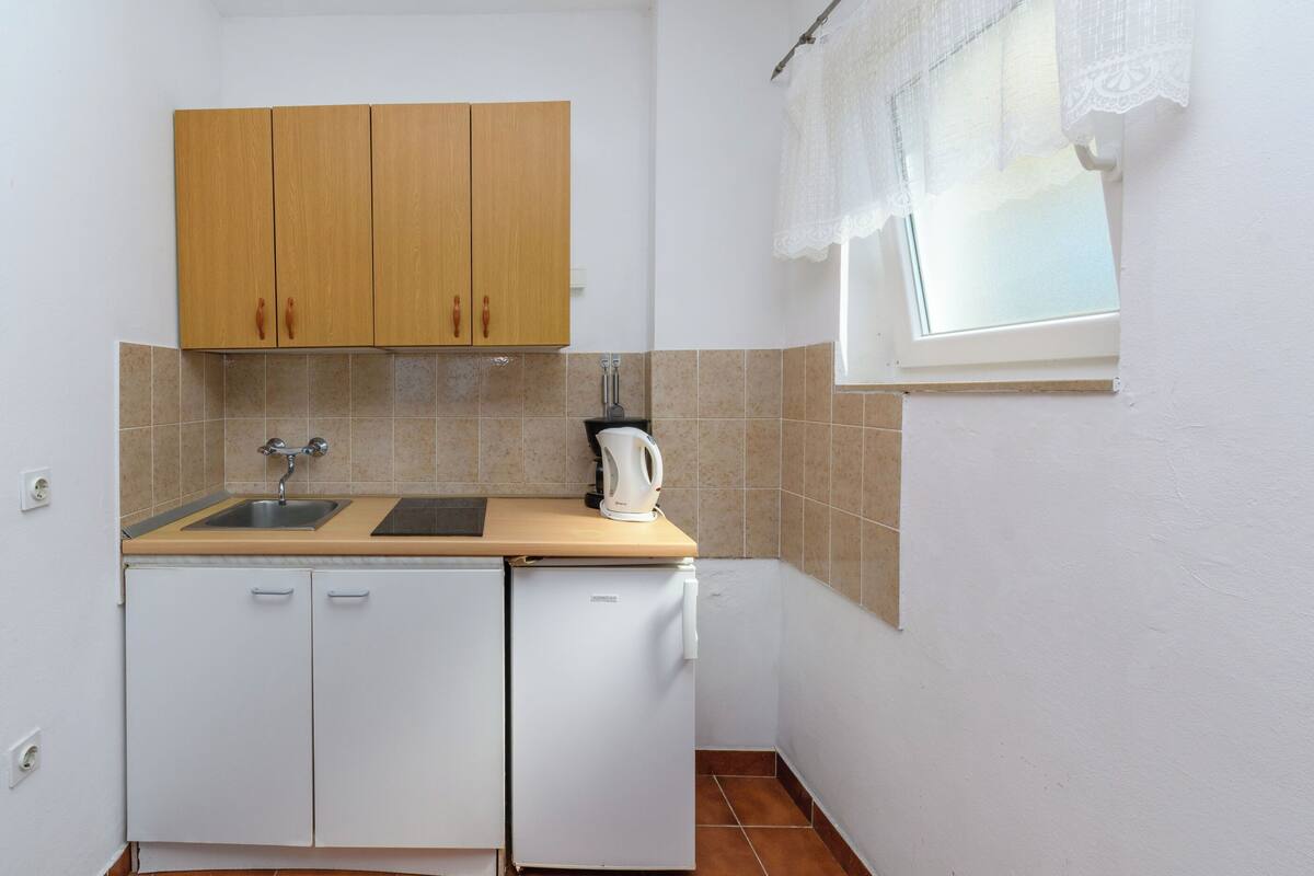 Una cocina compacta con un lavamanos, armarios de madera, un refrigerador blanco y una ventana con cortina blanca.