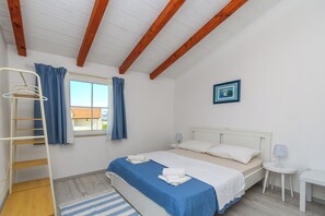 A bedroom with a bed, a window with curtains, a wooden ceiling, a small table, and a picture on the wall.
