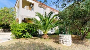 Edificio de dos plantas con tejado de tejas, escalinata de piedra y jardín cuidado con palmera y arbustos.