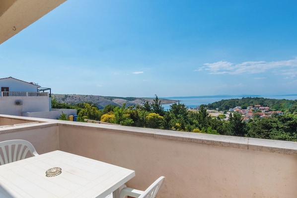 Un balcon avec une table et des chaises, donnant sur un paysage côtier avec des bâtiments et de la végétation.