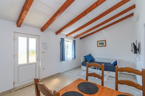 A room with a wooden table, a bench, a bed with a blue pillow, and a window with curtains.