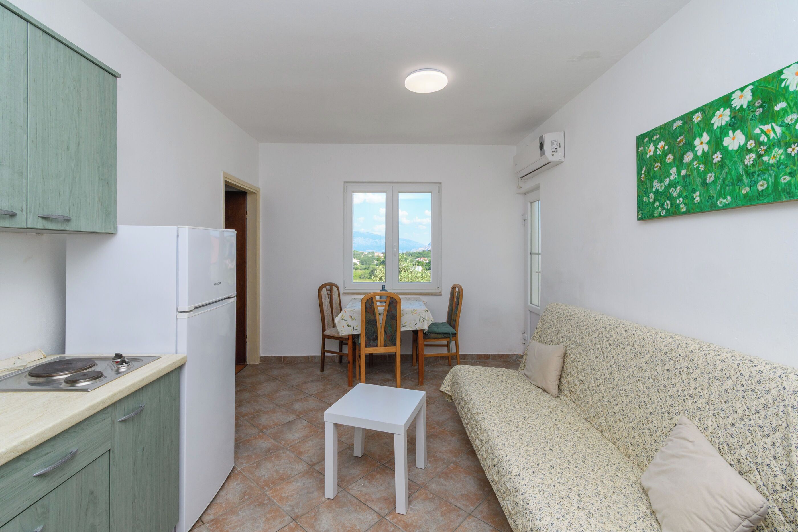A compact room with a kitchenette, a dining area with chairs, a sofa, and a window with a view.