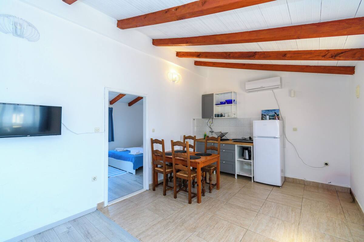 Un espacio habitable compacto con zona de comedor, kitchenette y televisor montado en la pared.
