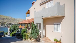 A coastal building with a balcony, steps leading to the entrance, and a view of the sea and hills in the background. - Apartments Vinka (Grebastica)