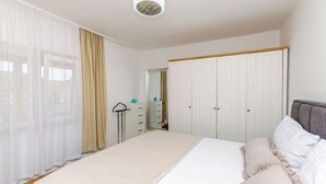A bedroom with a bed, a wardrobe, a mirror, and a window with curtains. - Apartments Vinka (Grebastica)