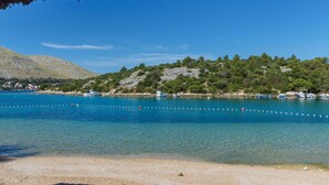 A coastal area with clear blue water, boats, and a rocky hill with trees. - Apartments Vinka (Grebastica)
