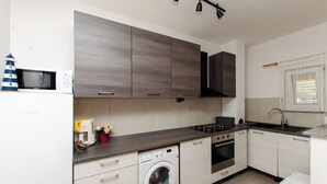 A modern kitchen with built-in appliances, a washing machine, and a microwave. - Apartments Vinka (Grebastica)