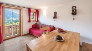 Une pièce comprenant une table à manger en bois, un canapé rouge, un balcon avec vue sur la campagne et des œuvres d’art décoratives accrochées au mur.