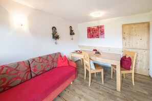 Una habitación con un sofá rojo, una mesa de comedor de madera, sillas, un armario de madera y adornos en la pared.