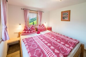 Un dormitorio con cama, almohadas, una ventana, un cuadro en la pared y una mesita de noche.
