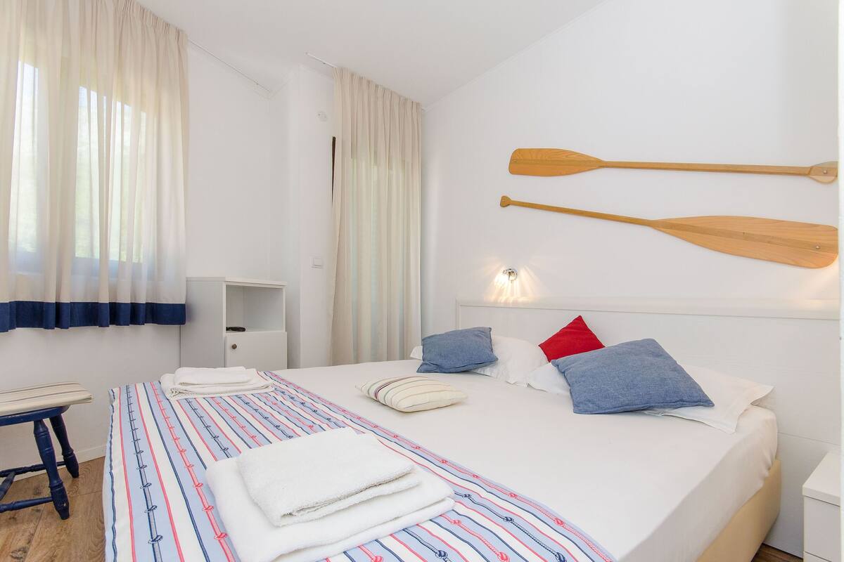 A neatly made bed with a striped bedspread, a bedside table, and two wooden paddles on the wall.