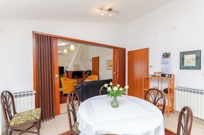 A dining area with a table, chairs, a vase of flowers, a wooden door, and a mirror reflecting the room. - Apartments Beach House Paradiso (Podgora)