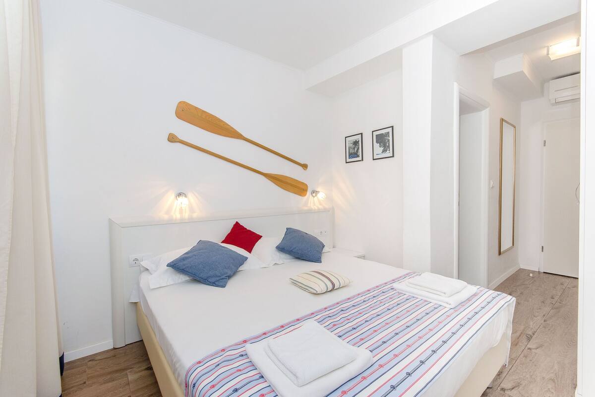 A neatly made bed with a striped bedspread, two pillows, and two wooden paddles hanging above.
