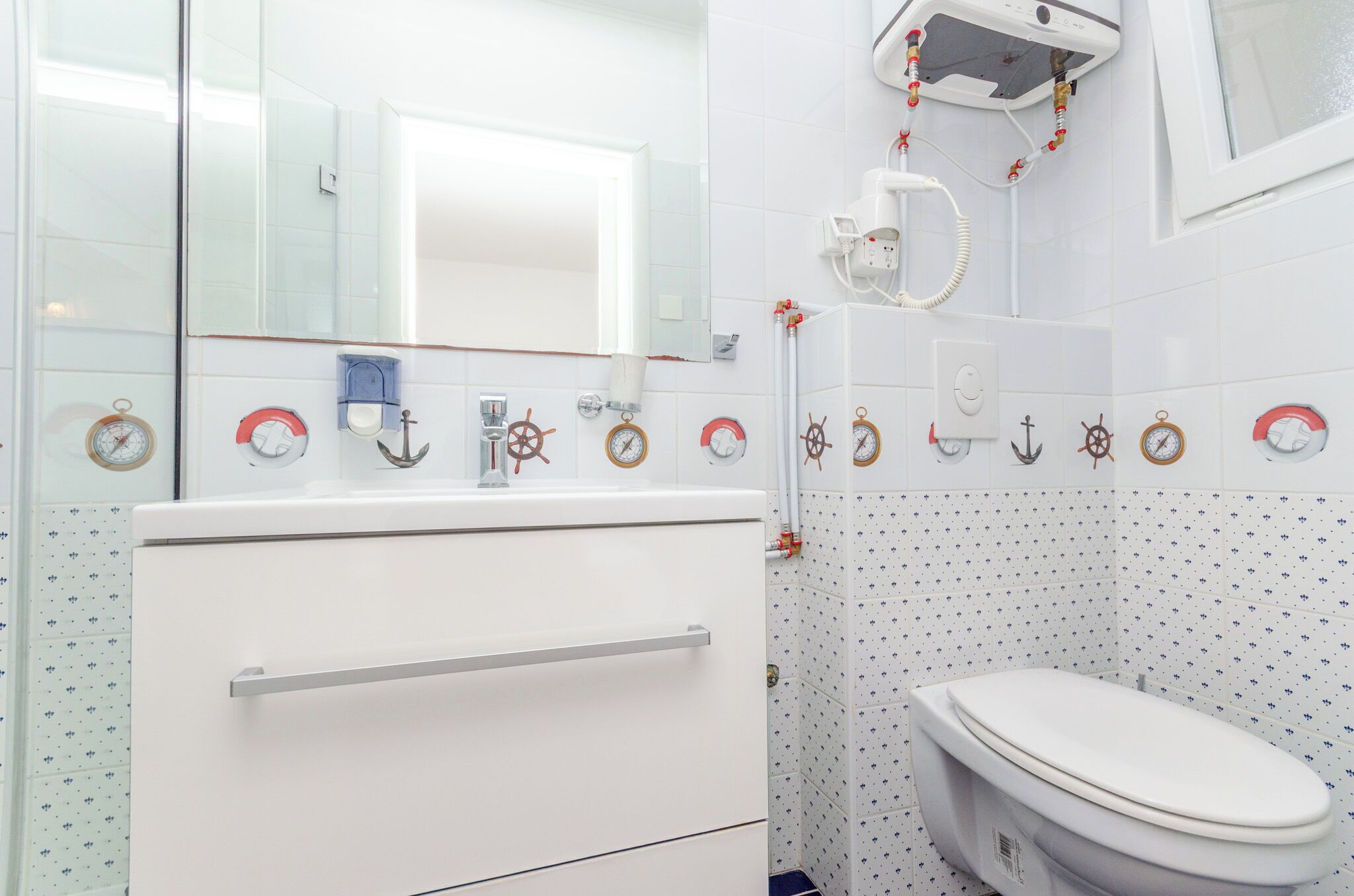 Un baño con lavamanos blanco, un espejo, un inodoro y decoración de paredes con motivos náuticos.