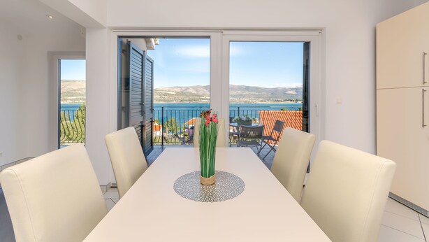 Spiseområde med et bord, stole og udsigt til en balkon med en pool.