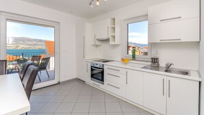 Et moderne køkken med hvide skabe, indbygget ovn og et stort vindue med udsigt til et smukt landskab.