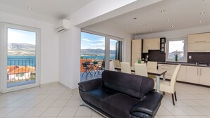 En rummelig opholdsstue med en sort sofa, et spisebord med stole og et køkkenområde med skabe og et vindue.