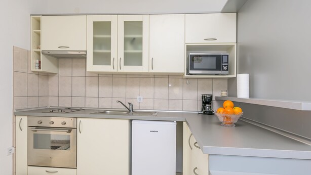 A compact kitchen with white cabinets, a built-in microwave, a small refrigerator, and a bowl of oranges on the counter. - Apartments Villa J i M by the sea (Stupin Celine)