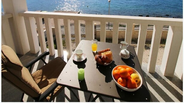 Un balcon avec une table préparée pour le petit-déjeuner, d’où l’on peut admirer un plan d’eau et une colline lointaine.