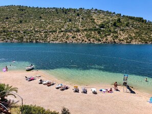 A beach with clear water, sun loungers, and a boat.