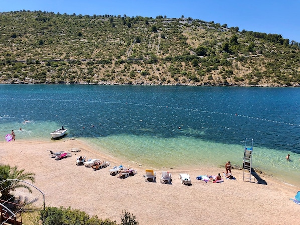 A beach with clear water, sun loungers, and a boat.