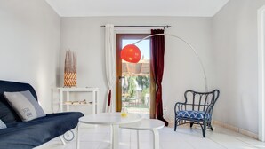 Uma sala de estar moderna com sofá, uma mesinha, uma cadeira e vista através de uma porta.