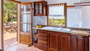 A kitchen with wooden cabinets, a sink, and a window with curtains. - Country House 'Sa Carbona' with Mountain View, Wi-Fi and Air Conditioning (Artá)