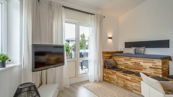 A modern living room with a flat-screen TV, a wooden bench with cushions, a sofa, and a large window with curtains.