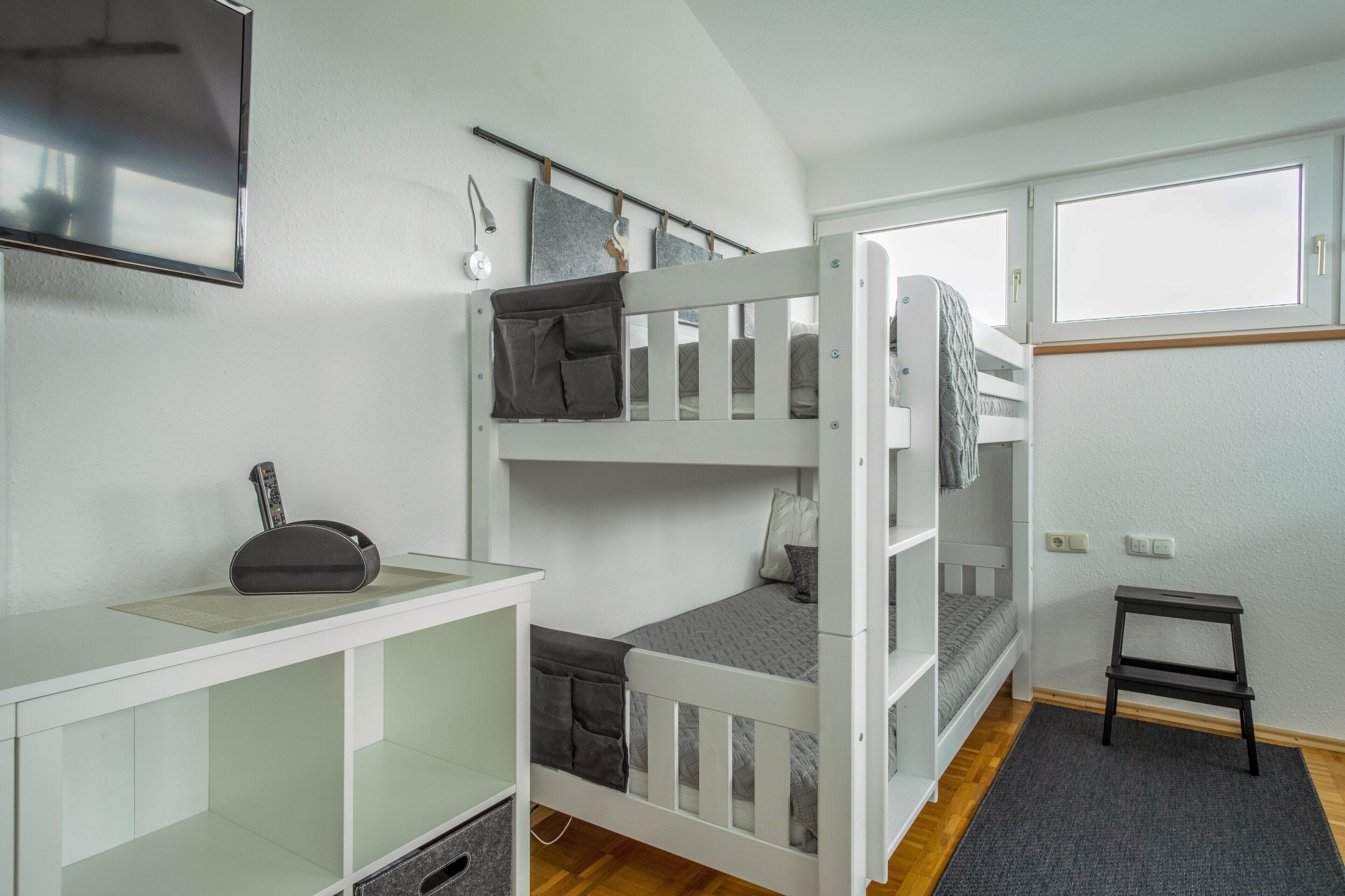 Une chambre avec un lit superposé, un bureau, une petite table et une fenêtre.
