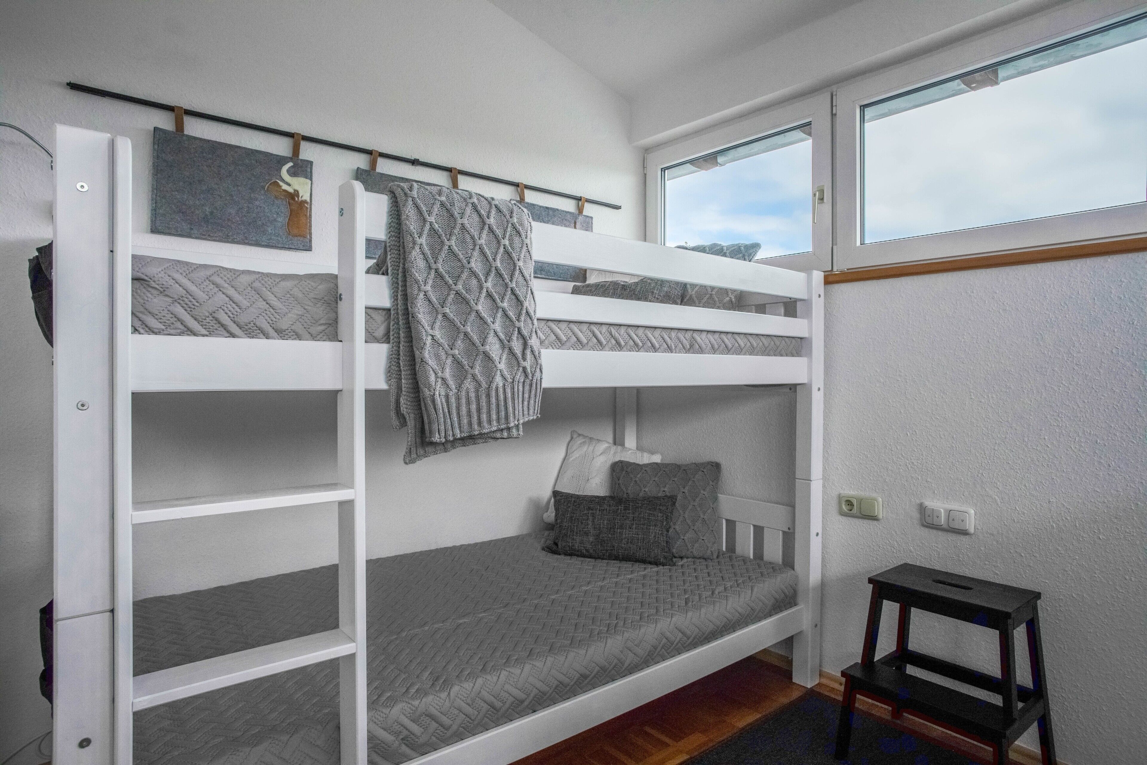 A bunk bed room with a window, a small table, and a wall-mounted shelf.