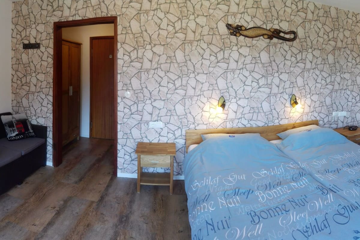 A bedroom with a bed, a desk, a chair, a wardrobe, and a painting on the wall.