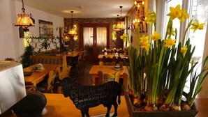 A restaurant interior with wooden tables and chairs, hanging lamps, and a blackboard with menu items. - Pension Talblick (Baiersbronn)