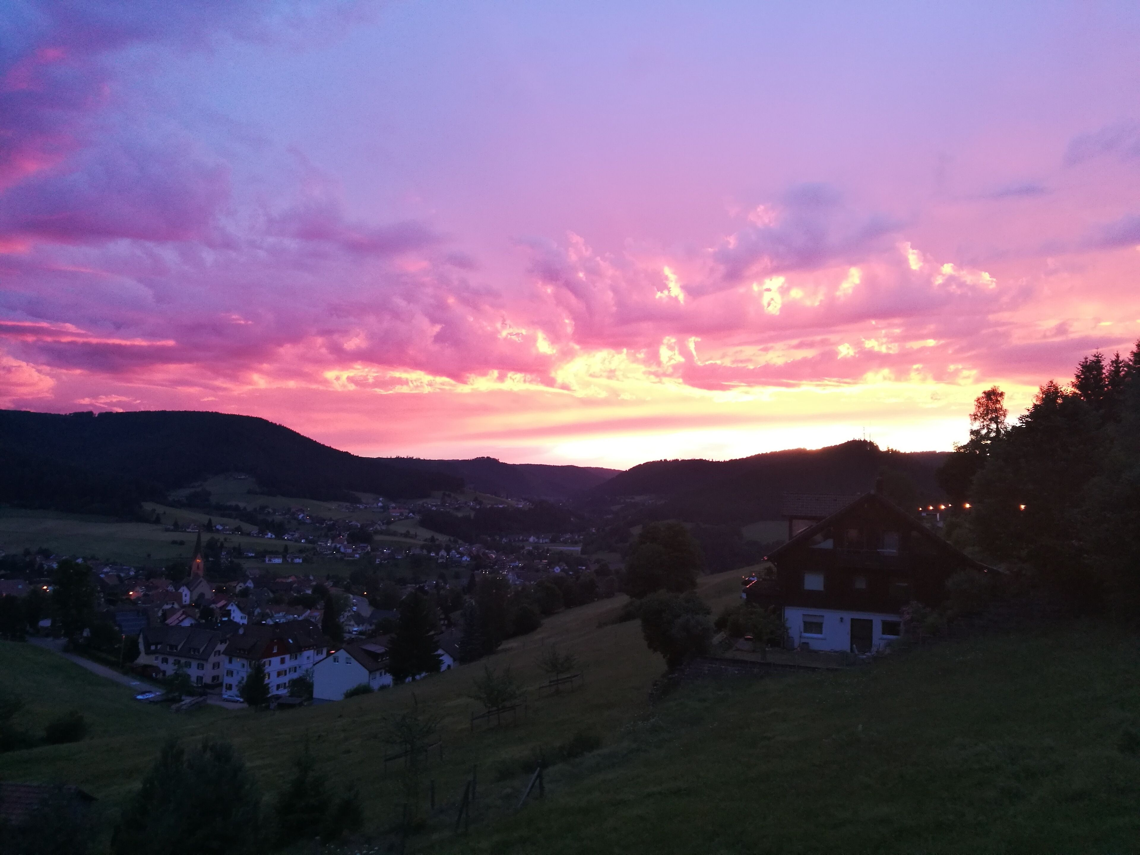 Un paisaje rural con un pueblo, colinas onduladas y un atardecer.